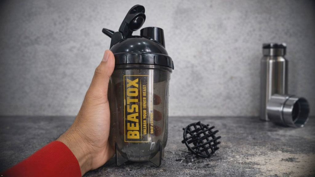 Hand holding NIGHTFURY Protein Shaker Bottle by BEASTOX with mixing ball on countertop, highlighting its ergonomic grip and compact size.